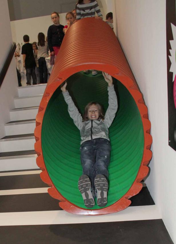 Ein Mädchen rutscht lachend eine orangefarbene Röhrenrutsche hinunter.