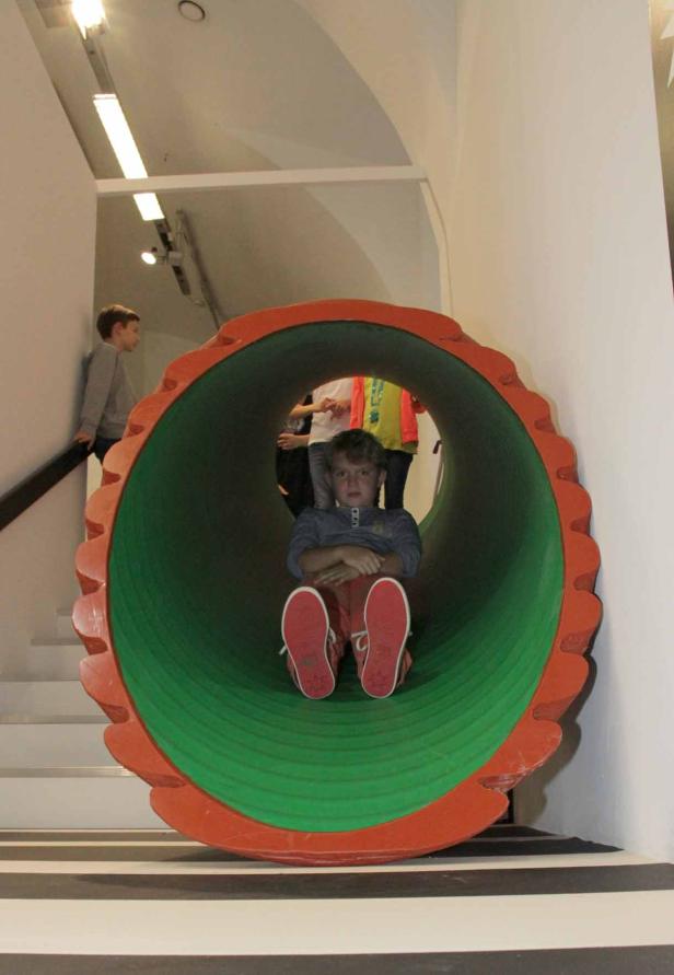 Ein Junge sitzt in einer grünen und orangefarbenen Röhre.
