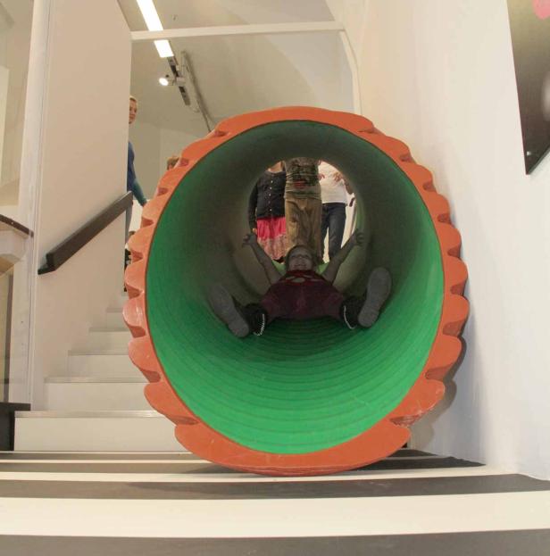 Ein Kind rutscht in einem grünen Tunnel mit orangefarbenen Rändern.