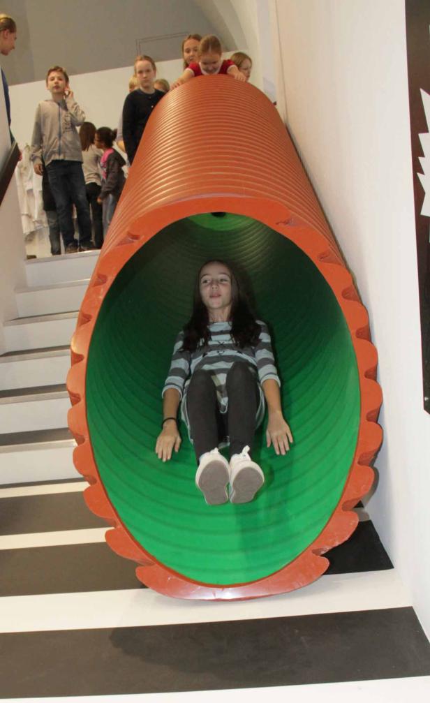 Ein Mädchen rutscht eine orangefarbene Röhrenrutsche hinunter.