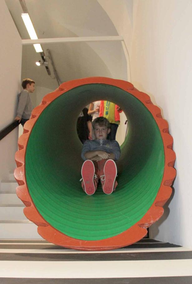 Ein Junge sitzt in einer großen, grünen Röhre mit rotem Rand.