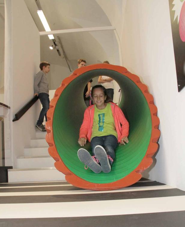 Ein Mädchen rutscht in einem orangefarbenen und grünen Tunnel herunter.