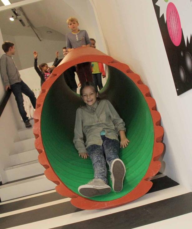 Ein Mädchen rutscht in einer grünen Röhre, während andere Kinder zusehen.