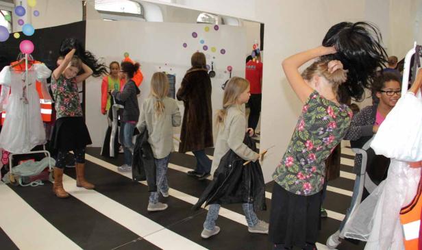 Mehrere Mädchen probieren in einem Raum Kleider und Perücken an.