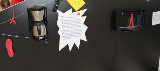 Eine Kaffeemaschine, eine rote Sandale, ein Eiffelturm-Modell und ein Bildschirm auf einer schwarzen Oberfläche.