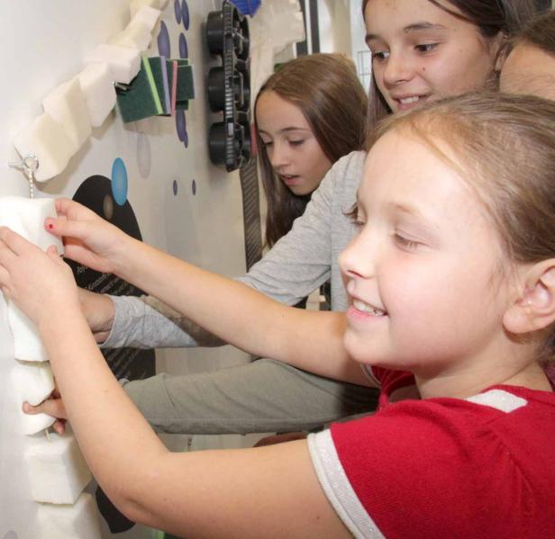 Drei Mädchen betrachten und berühren eine Installation aus Schaumstoff und anderen Materialien.