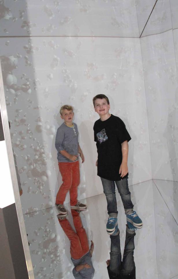 Zwei Jungen stehen in einem Raum mit Spiegelboden und gemusterter Wand.