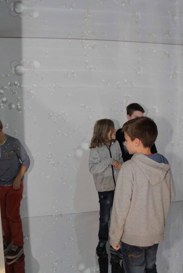 Eine Gruppe von Kindern steht vor einer Wand mit einem Muster aus Moleküldarstellungen.