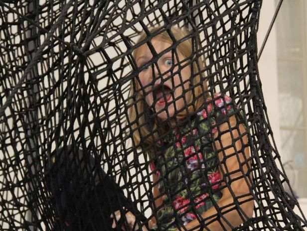 Ein Mädchen mit offenem Mund klettert in einem schwarzen Netz.