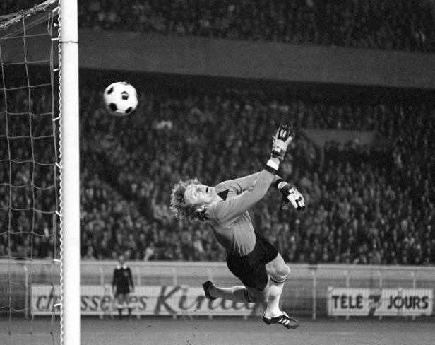 Ein Torwart springt, um einen Fußball vor einem vollen Stadion zu fangen.
