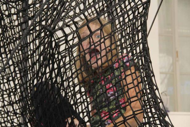 Ein Mädchen schaut mit aufgerissenem Mund und großen Augen durch ein schwarzes Netz.