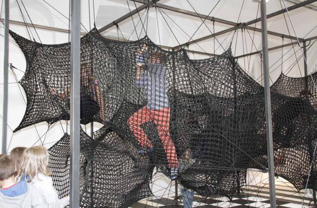 Kinder klettern in einer großen, netzartigen Kletterstruktur.