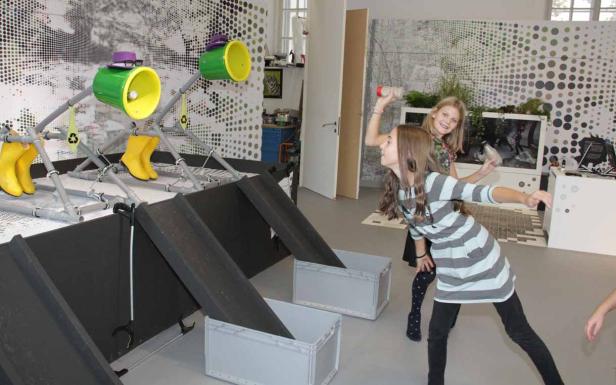 Zwei Mädchen werfen Plastikflaschen in eine Recycling-Installation.