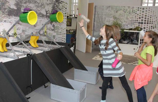 Mädchen werfen Plastikflaschen in ein Recycling-Spiel.