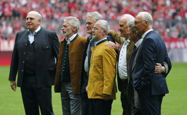 Eine Gruppe älterer Herren steht auf einem Fußballfeld, einige tragen Trachtenjacken.