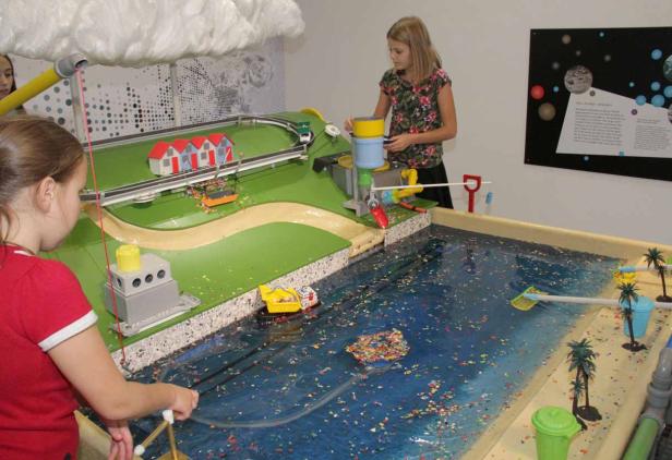 Zwei Mädchen spielen mit einem interaktiven Modell, das Wasserverschmutzung darstellt.