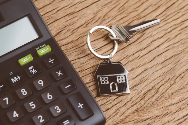 Mortgage calculation or buy and sell house, property and real estate, home key with house keyring or keychain with black calculator on wooden table