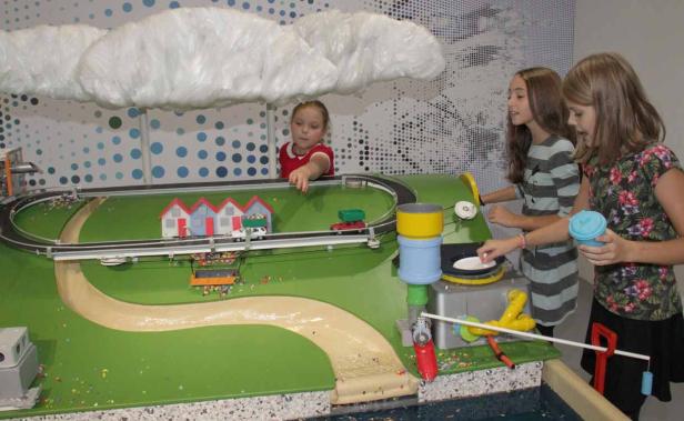 Drei Mädchen spielen mit einem interaktiven Modell einer Stadt und einer Wolke.