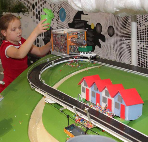 Ein Mädchen befüllt eine Recyclinganlage mit einem grünen Eimer.