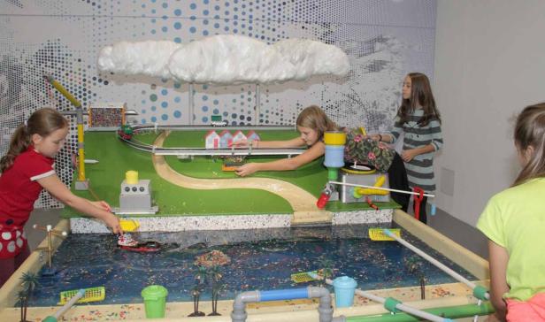 Mehrere Mädchen spielen mit einem interaktiven Modell einer Stadt mit einem Fluss.