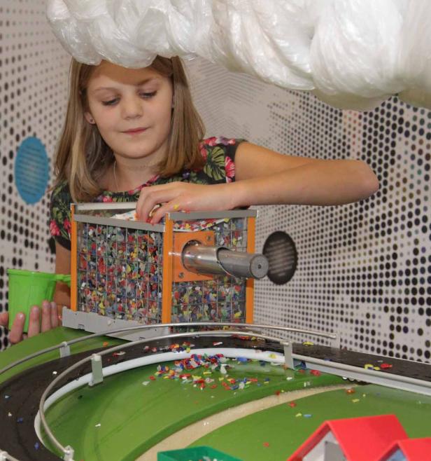 Ein Mädchen befüllt eine Maschine mit bunten Plastikstücken.