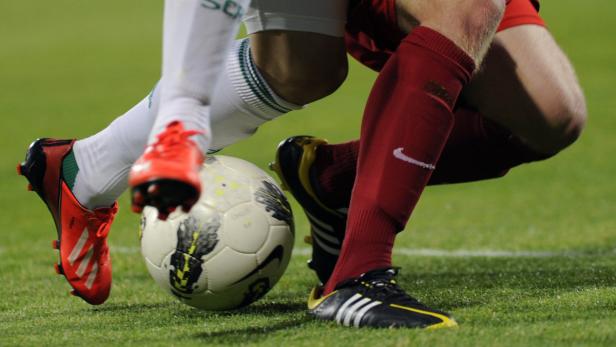 Zwei Fußballspieler kämpfen um den Ball auf dem grünen Rasen.