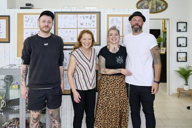 Eine Gruppe von vier Personen steht in einem Tattoo-Studio und lächelt in die Kamera.
