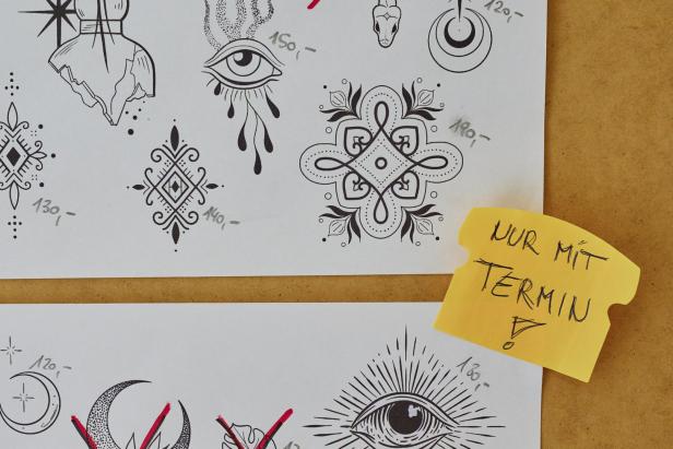 Ein Blatt Papier mit verschiedenen Tattoo-Vorlagen und einem gelben Zettel mit der Aufschrift „Nur mit Termin“.