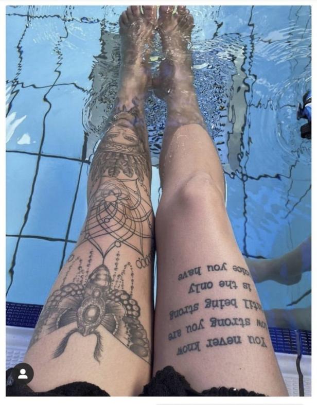 Beine einer Person mit Tätowierungen im Wasser.