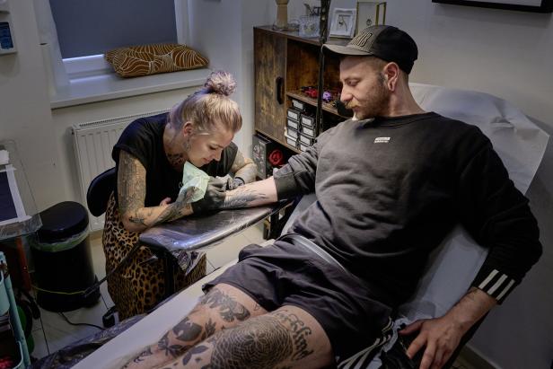 Eine Tätowiererin sticht einem Mann ein Tattoo auf den Unterarm.
