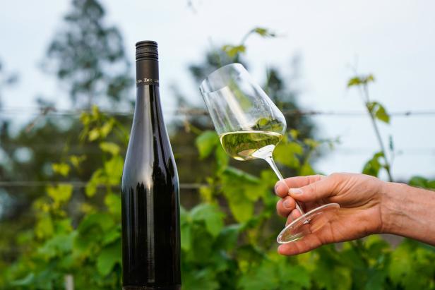 Eine Flasche Weißwein und ein Weinglas werden vor einem Weinberg präsentiert.