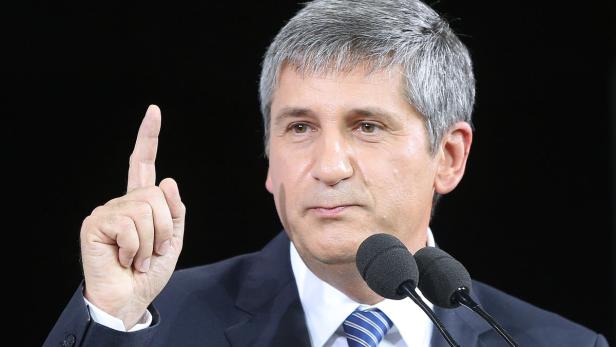 Ein Mann in einem Anzug gestikuliert mit erhobenem Zeigefinger vor zwei Mikrofonen.