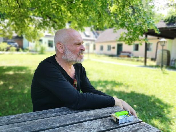 Ein Mann mit Bart sitzt an einem Tisch im Freien.
