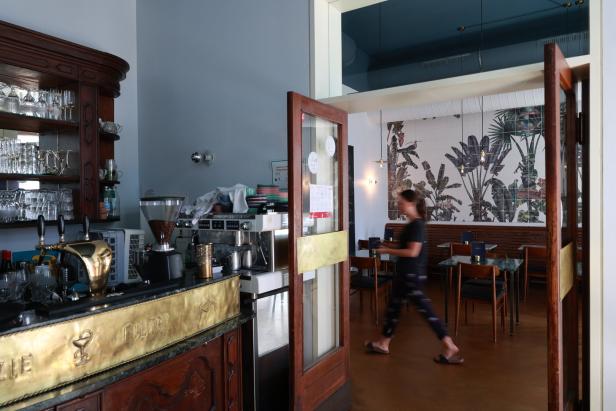 Eine Frau betritt ein Café mit einer Wand voller tropischer Pflanzenmuster.