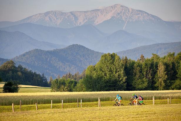 Eine Gruppe von Radfahrern fährt durch eine ländliche Landschaft mit Bergen im Hintergrund.
