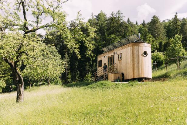Ein Tiny House mit Solardach steht auf einer grünen Wiese am Waldrand.