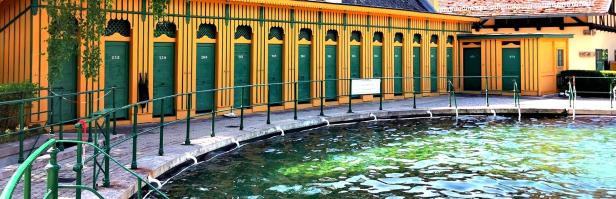 Ein Freibad mit gelb-grünen Umkleidekabinen und einem Becken mit klarem Wasser.