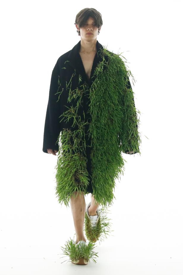Ein Model auf dem Laufsteg trägt einen Mantel mit Grasbewuchs und passende Schuhe von Loewe.
