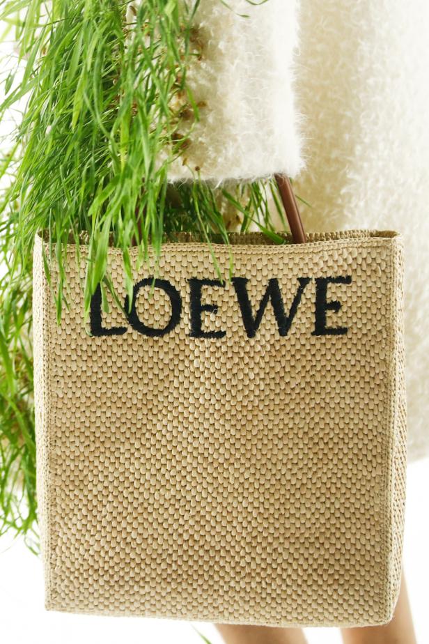 Eine „Loewe“-Tasche aus Bast mit grünen Pflanzen darin wird getragen.