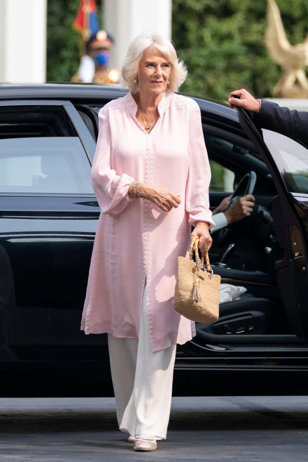 Königin Camilla verlässt ein schwarzes Auto mit einer hellrosa Tunika und einer Basttasche.