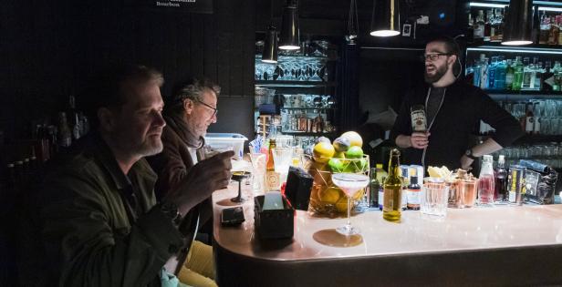Zwei Männer sitzen an einer Bar, während ein Barkeeper einen Drink zubereitet.