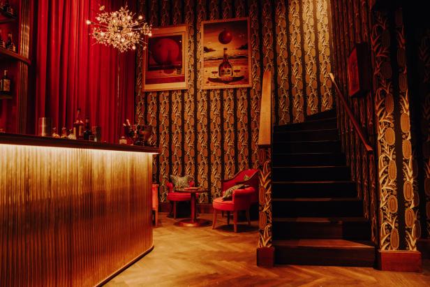 Eine Bar mit roten Vorhängen, gemusterter Tapete und einer Treppe.