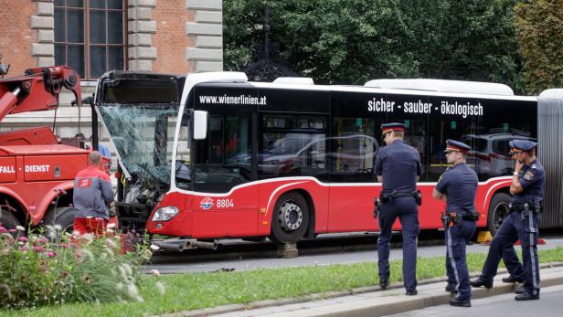 Ein beschädigter Bus der Wiener Linien wird von einem Abschleppwagen geborgen, während Polizisten die Szene beobachten.