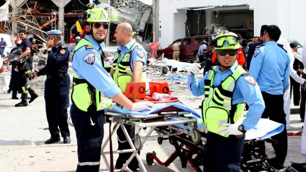 Rettungskräfte stehen vor einem beschädigten Gebäude mit einem Krankenwagen bereit.