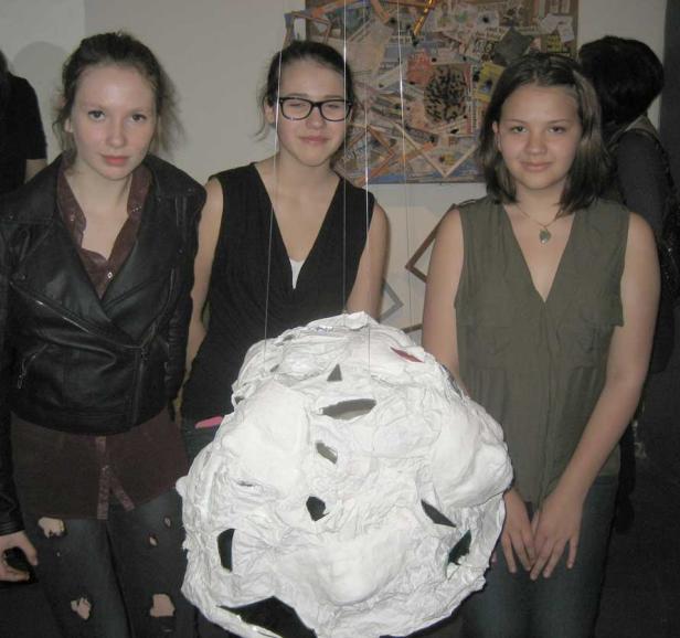 Drei junge Frauen stehen vor einer Kunstinstallation aus Papier.
