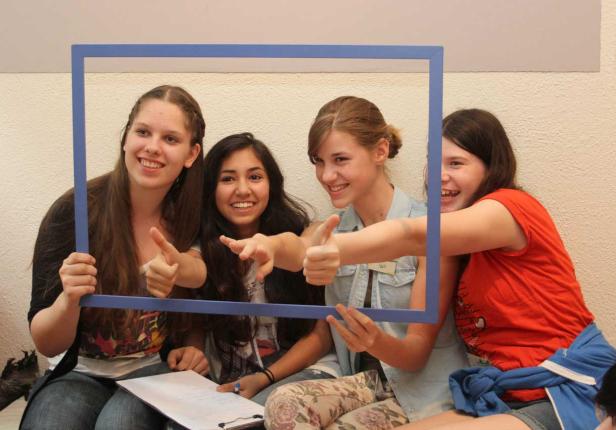 Vier junge Frauen halten einen blauen Rahmen und zeigen mit den Daumen nach oben.