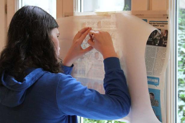 Eine Person zeichnet ein Bild ab, das an einem Fenster befestigt ist.