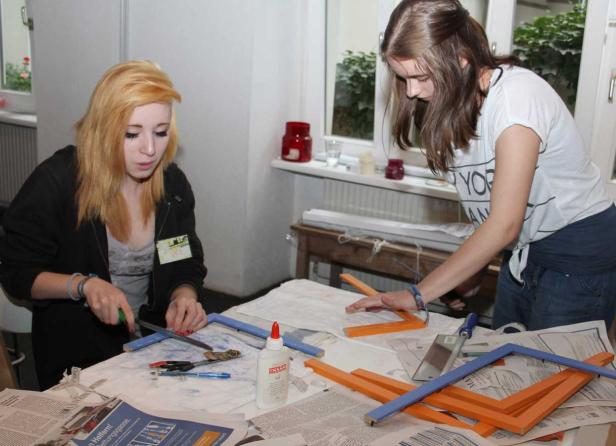 Zwei junge Frauen basteln an einem Tisch mit farbigen Holzrahmen.