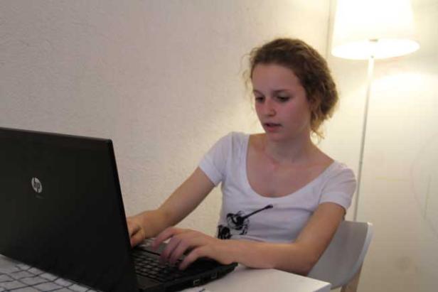 Eine junge Frau sitzt an einem Tisch und tippt auf einem Laptop.