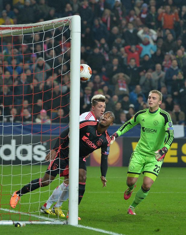 Ein Fußballspieler köpft den Ball vor dem Tor, während der Torwart zusieht.